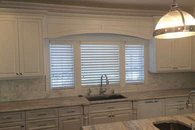 Inspiration for a large coastal l-shaped enclosed kitchen remodel in New York with an undermount sink, raised-panel cabinets, white cabinets, marble countertops, white backsplash, stone tile backsplash, stainless steel appliances and an island