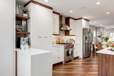 Example of a mid-sized transitional galley medium tone wood floor and brown floor open concept kitchen design in Calgary with flat-panel cabinets, white cabinets, quartzite countertops, gray backsplash, stone tile backsplash, stainless steel appliances and an island
