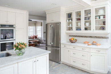 Example of a mid-sized transitional u-shaped marble floor and white floor eat-in kitchen design in New York with a drop-in sink, glass-front cabinets, white cabinets, marble countertops, white backsplash, subway tile backsplash, stainless steel appliances and an island
