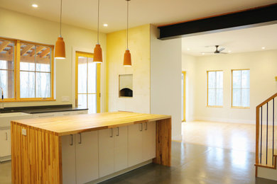 Example of a mid-sized danish l-shaped concrete floor and gray floor kitchen design in Other with a farmhouse sink, flat-panel cabinets, white cabinets, wood countertops, white backsplash, stainless steel appliances, an island and brown countertops