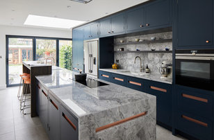 This is an example of a large contemporary single-wall kitchen in London with a built-in sink, flat-panel cabinets, blue cabinets, granite worktops, grey splashback, marble splashback, stainless steel appliances, ceramic flooring, an island, grey floors and grey worktops.