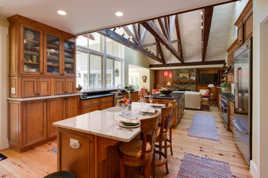 Bild på ett stort amerikanskt kök, med en rustik diskho, luckor med infälld panel, skåp i mellenmörkt trä, granitbänkskiva, rostfria vitvaror, ljust trägolv, flera köksöar och brunt golv