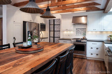 This is an example of a rustic u-shaped open plan kitchen in Seattle with shaker cabinets, white cabinets, wood worktops, an island, a belfast sink, white splashback, metro tiled splashback, stainless steel appliances and medium hardwood flooring.