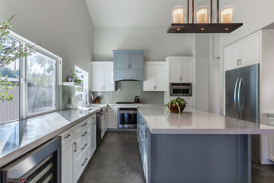 Example of a large transitional u-shaped porcelain tile and gray floor eat-in kitchen design in Los Angeles with shaker cabinets, white cabinets, quartz countertops, green backsplash, glass tile backsplash, stainless steel appliances, an island, white countertops and a farmhouse sink