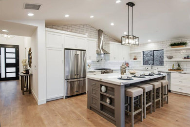 Medium sized modern l-shaped open plan kitchen in Los Angeles with a submerged sink, shaker cabinets, white cabinets, engineered stone countertops, white splashback, metro tiled splashback, stainless steel appliances, light hardwood flooring, an island, brown floors and white worktops.