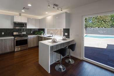 Mid-sized trendy l-shaped dark wood floor and brown floor eat-in kitchen photo in Los Angeles with an undermount sink, flat-panel cabinets, white cabinets, quartz countertops, gray backsplash, porcelain backsplash, stainless steel appliances and a peninsula