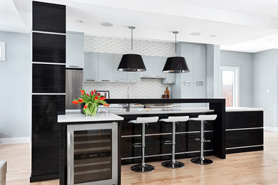 Design ideas for a large contemporary galley open plan kitchen in Ottawa with a submerged sink, flat-panel cabinets, black cabinets, engineered stone countertops, white splashback, ceramic splashback, stainless steel appliances, an island, beige floors and light hardwood flooring.