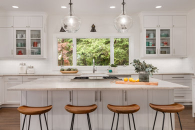 Kitchen - large transitional medium tone wood floor and brown floor kitchen idea in Seattle with a farmhouse sink, shaker cabinets, white cabinets, granite countertops, white backsplash, subway tile backsplash, stainless steel appliances, beige countertops and an island