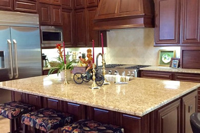 Example of a mid-sized classic l-shaped porcelain tile eat-in kitchen design in Austin with an undermount sink, raised-panel cabinets, dark wood cabinets, granite countertops, beige backsplash, stainless steel appliances and an island