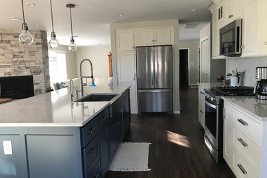 Kitchen - transitional brown floor kitchen idea in Cedar Rapids with a farmhouse sink, beaded inset cabinets, white cabinets, quartz countertops, gray backsplash, porcelain backsplash, stainless steel appliances, an island and white countertops