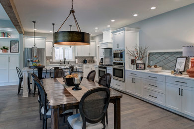 Example of a large cottage l-shaped brown floor open concept kitchen design in Portland with a farmhouse sink, white cabinets, gray backsplash, subway tile backsplash, stainless steel appliances and an island