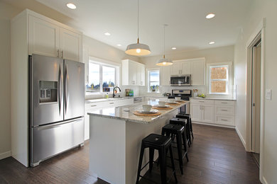 Example of a large arts and crafts l-shaped dark wood floor open concept kitchen design in Seattle with an undermount sink, shaker cabinets, white cabinets, granite countertops, white backsplash, subway tile backsplash, stainless steel appliances and an island