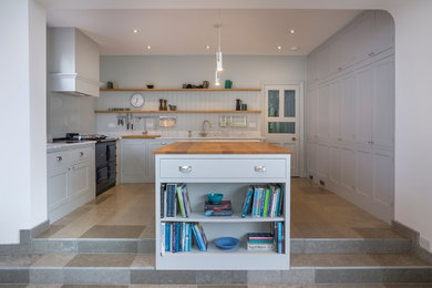 This is an example of a large contemporary u-shaped open plan kitchen in Oxfordshire with a belfast sink, shaker cabinets, grey cabinets, composite countertops, white splashback, integrated appliances, ceramic flooring and an island.