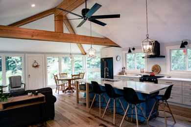 Inspiration for a mid-sized modern single-wall medium tone wood floor and brown floor open concept kitchen remodel in Other with an undermount sink, shaker cabinets, white cabinets, black appliances, an island and white countertops