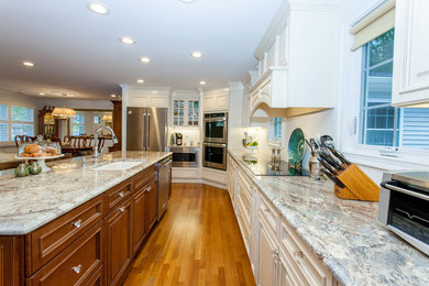 Example of a large classic l-shaped medium tone wood floor open concept kitchen design in Orange County with a single-bowl sink, raised-panel cabinets, white cabinets, granite countertops, stainless steel appliances and an island
