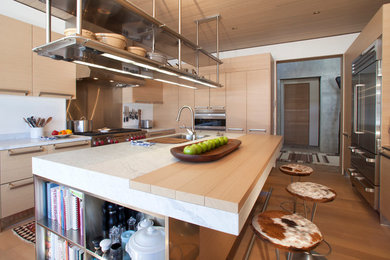 Eat-in kitchen - mid-sized modern l-shaped medium tone wood floor eat-in kitchen idea in Denver with flat-panel cabinets, light wood cabinets, stainless steel appliances, an island, a drop-in sink, tile countertops and metallic backsplash