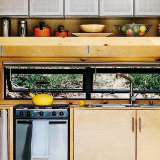 This is an example of a small country single-wall open plan kitchen in Denver with a double-bowl sink, flat-panel cabinets, light wood cabinets, stainless steel appliances, no island, wood benchtops and window splashback.