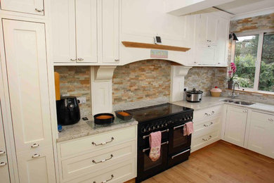 This is an example of a large classic l-shaped kitchen/diner in Other with a double-bowl sink, shaker cabinets, beige cabinets, composite countertops, multi-coloured splashback, stone tiled splashback, black appliances, medium hardwood flooring and an island.