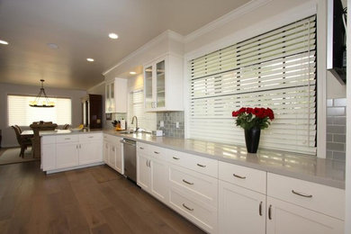 Example of a large transitional l-shaped medium tone wood floor and brown floor eat-in kitchen design in Los Angeles with an undermount sink, shaker cabinets, white cabinets, soapstone countertops, metallic backsplash, subway tile backsplash, stainless steel appliances and a peninsula
