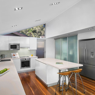 Design ideas for a contemporary u-shaped separate kitchen in Sydney with an undermount sink, flat-panel cabinets, white cabinets, white splashback, glass sheet splashback, stainless steel appliances, medium hardwood floors, with island and brown floor.
