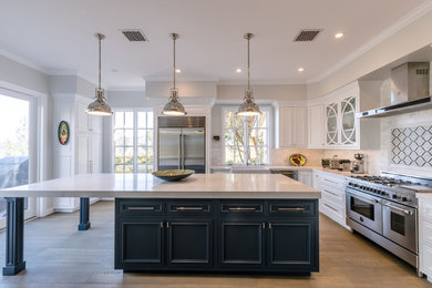Inspiration for a large traditional l-shaped kitchen in Los Angeles with a belfast sink, recessed-panel cabinets, white cabinets, stainless steel appliances, medium hardwood flooring and an island.