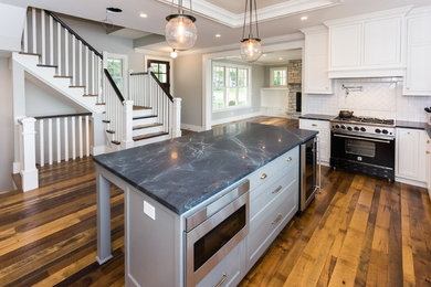 Large transitional u-shaped dark wood floor and brown floor open concept kitchen photo in Minneapolis with a farmhouse sink, shaker cabinets, white cabinets, granite countertops, white backsplash, subway tile backsplash and white appliances