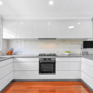Photo of a mid-sized contemporary u-shaped open plan kitchen in Brisbane with a drop-in sink, flat-panel cabinets, white cabinets, quartz benchtops, multi-coloured splashback, porcelain splashback, stainless steel appliances, medium hardwood floors, a peninsula and orange floor.
