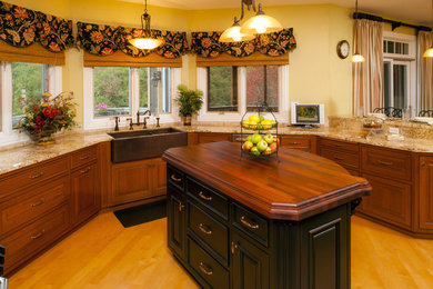 Example of a large classic u-shaped dark wood floor enclosed kitchen design in Chicago with a farmhouse sink, raised-panel cabinets, dark wood cabinets, granite countertops, beige backsplash, stone tile backsplash, stainless steel appliances and an island