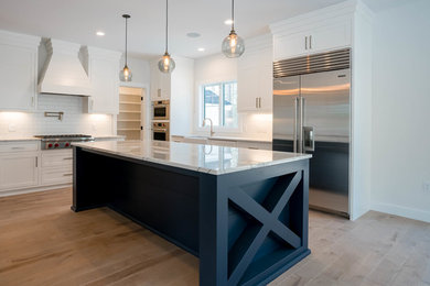 Eat-in kitchen - large farmhouse l-shaped light wood floor and brown floor eat-in kitchen idea in Other with a farmhouse sink, shaker cabinets, white cabinets, quartzite countertops, white backsplash, subway tile backsplash, stainless steel appliances, an island and white countertops