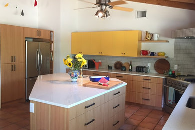 Photo of a medium sized eclectic u-shaped open plan kitchen in Phoenix with a submerged sink, flat-panel cabinets, yellow cabinets, engineered stone countertops, grey splashback, matchstick tiled splashback, stainless steel appliances, travertine flooring, an island and brown floors.