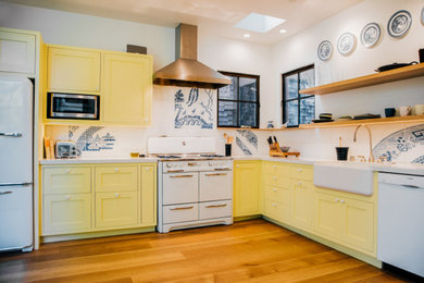 Inspiration for a large eclectic l-shaped medium tone wood floor and brown floor kitchen pantry remodel in San Francisco with a farmhouse sink, shaker cabinets, yellow cabinets, white backsplash, porcelain backsplash, white appliances, no island and white countertops