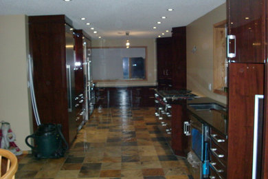 Photo of a large contemporary galley kitchen/diner in Calgary with a submerged sink, granite worktops, slate flooring, raised-panel cabinets, dark wood cabinets and stainless steel appliances.