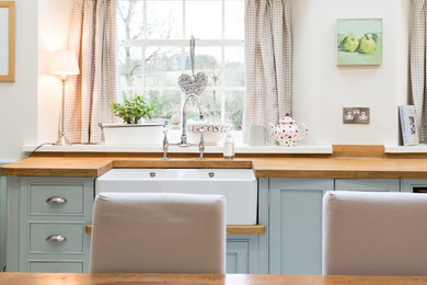 Photo of a medium sized country l-shaped kitchen/diner in Other with a belfast sink, shaker cabinets, blue cabinets, wood worktops, white splashback, white appliances and no island.