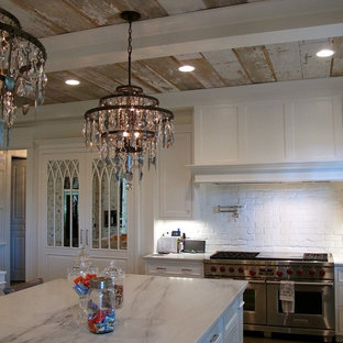 Réalisation d'une grand cuisine américaine style shabby chic en L avec un évier de ferme, un placard à porte shaker, des portes de placard blanches, un plan de travail en marbre, une crédence blanche, une crédence en brique, un électroménager en acier inoxydable, un sol en bois foncé, un îlot central et un sol marron.