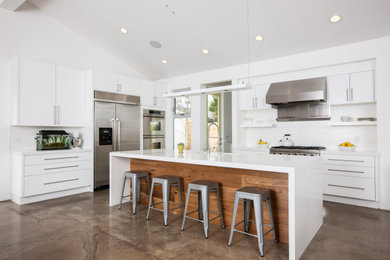 Trendy l-shaped concrete floor, gray floor and vaulted ceiling kitchen photo in Orange County with an undermount sink, flat-panel cabinets, white cabinets, white backsplash, stainless steel appliances, an island and white countertops