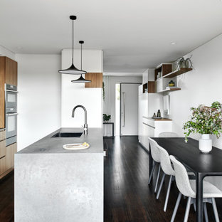 Ispirazione per una cucina moderna di medie dimensioni con lavello sottopiano, ante lisce, ante in legno scuro, top in vetro, paraspruzzi grigio, paraspruzzi in lastra di pietra, elettrodomestici neri, parquet scuro, penisola, pavimento nero e top grigio
