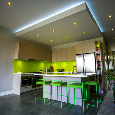 Example of a small trendy l-shaped concrete floor eat-in kitchen design in Sydney with flat-panel cabinets, light wood cabinets, green backsplash, stainless steel appliances, an undermount sink, solid surface countertops, glass sheet backsplash and an island