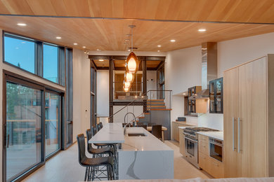 Cette photo montre une cuisine américaine moderne en bois clair avec un évier encastré, un placard à porte plane, un électroménager en acier inoxydable, îlot et un plan de travail blanc.