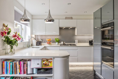 Inspiration for a medium sized contemporary u-shaped kitchen in Other with a submerged sink, flat-panel cabinets, white cabinets, grey splashback, stainless steel appliances, grey worktops, a breakfast bar and grey floors.