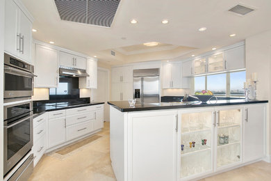 Large traditional l-shaped kitchen in Miami with a submerged sink, recessed-panel cabinets, white cabinets, granite worktops, black splashback, stone slab splashback, stainless steel appliances, travertine flooring, no island and beige floors.