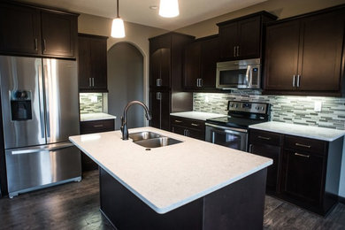 Mid-sized transitional u-shaped dark wood floor enclosed kitchen photo in Other with a double-bowl sink, shaker cabinets, dark wood cabinets, quartzite countertops, gray backsplash, matchstick tile backsplash, stainless steel appliances and an island