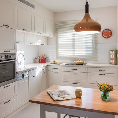 Elegant l-shaped kitchen photo in Tel Aviv with white cabinets, white backsplash, subway tile backsplash, stainless steel appliances and an island