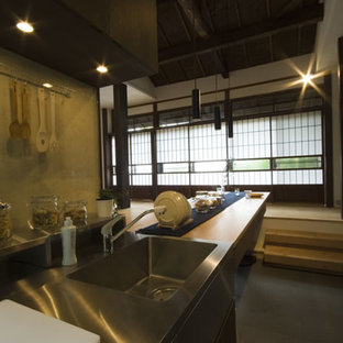 Mid-sized asian open concept kitchen ideas - Example of a mid-sized zen single-wall slate floor open concept kitchen design in Yokohama with an undermount sink, dark wood cabinets, stainless steel countertops, black appliances, an island and beige countertops