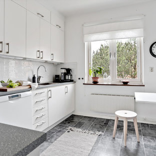 Minimalistisk inredning av ett kök och matrum, med släta luckor, vita skåp, vitt stänkskydd, laminatgolv, grått golv och vita vitvaror