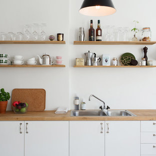 Diseño de cocina lineal, escandinava, de tamaño medio, sin isla, con puertas de armario blancas, electrodomésticos de acero inoxidable, fregadero de doble seno, armarios con paneles lisos y encimera de madera