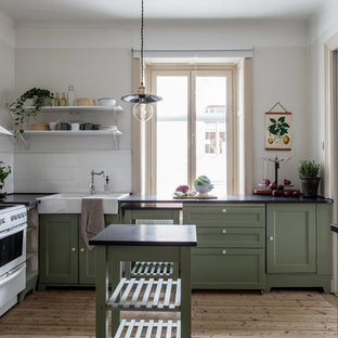 Inspiration för ett mellanstort, avskilt lantligt svart svart kök, med en rustik diskho, skåp i shakerstil, gröna skåp, vitt stänkskydd, vita vitvaror, ljust trägolv, en köksö och beiget golv