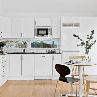 Idéer för minimalistiska svart kök, med en undermonterad diskho, släta luckor, vita skåp, vitt stänkskydd, stänkskydd i tunnelbanekakel, vita vitvaror, ljust trägolv och beiget golv