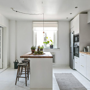 Idéer för avskilda minimalistiska brunt parallellkök, med släta luckor, vita skåp, träbänkskiva, vitt stänkskydd, rostfria vitvaror, målat trägolv, en köksö och vitt golv
