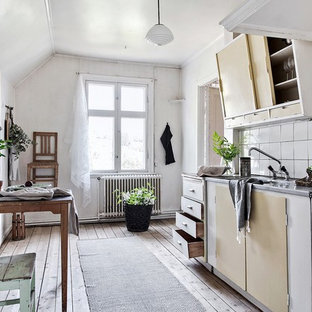 Bild på ett skandinaviskt grå linjärt grått kök och matrum, med en integrerad diskho, släta luckor, vita skåp, bänkskiva i rostfritt stål, vitt stänkskydd, vita vitvaror, ljust trägolv och beiget golv