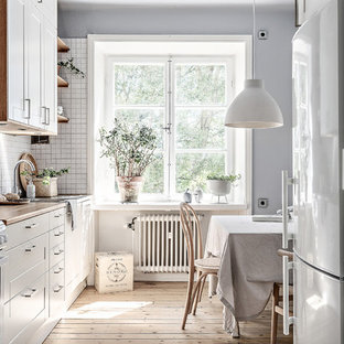 Inredning av ett minimalistiskt mellanstort beige beige kök och matrum, med vita skåp, träbänkskiva, vita vitvaror, ljust trägolv, beiget golv, en undermonterad diskho, vitt stänkskydd och skåp i shakerstil